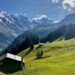 Alpine hiking landscape with a chalet, green meadows, and snowy peaks