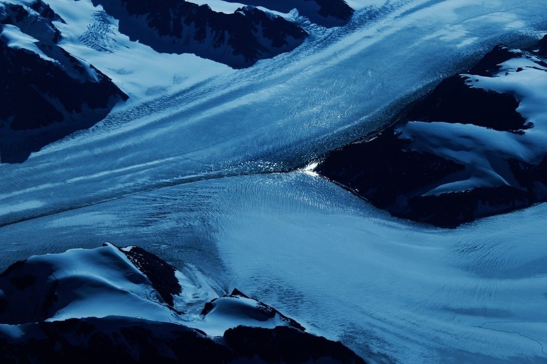 Aerial view of blue glacier ice flowing between snow-covered mountain ridges