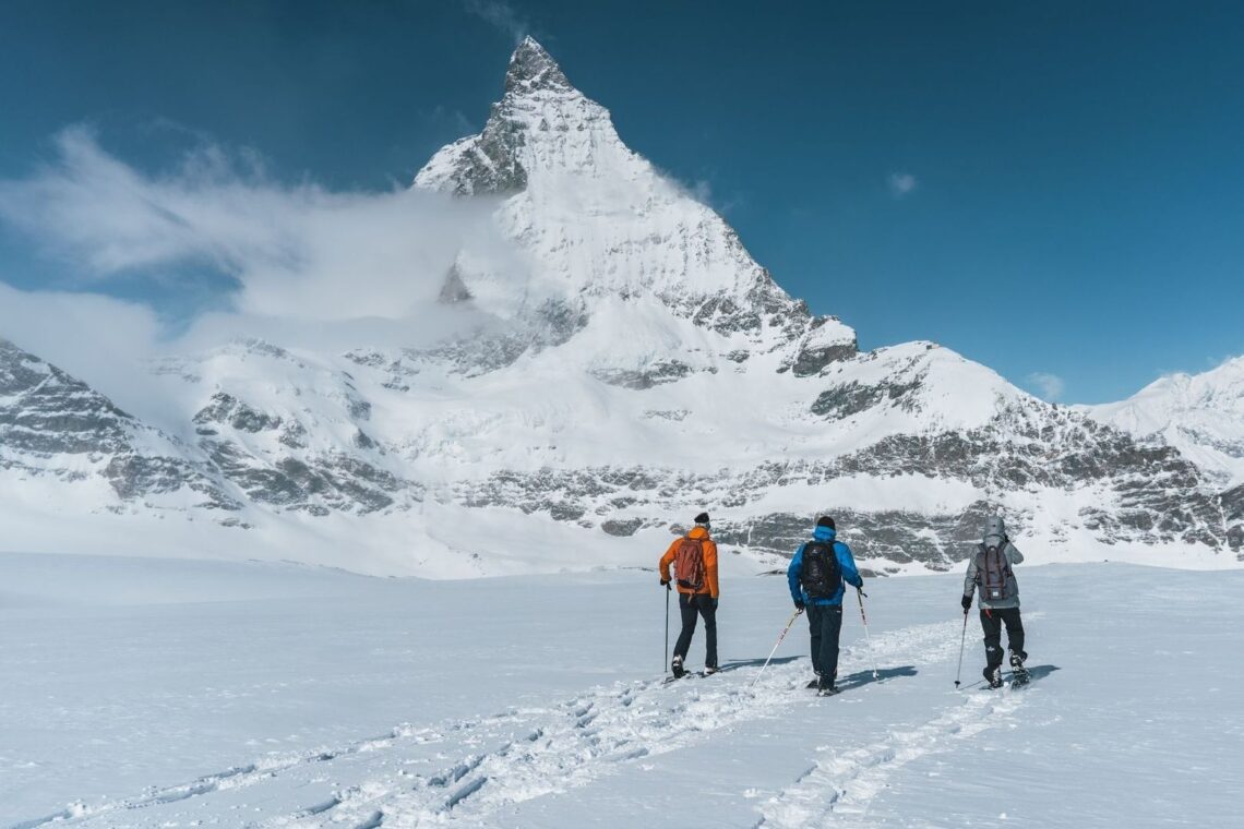 Three snowshoers crossing a snowy Alpine landscape beneath a peak