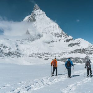 Three snowshoers crossing a snowy Alpine landscape beneath a peak