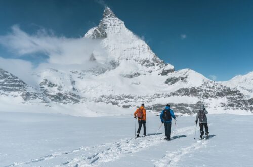 Three snowshoers crossing a snowy Alpine landscape beneath a peak