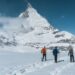 Three snowshoers crossing a snowy Alpine landscape beneath a peak