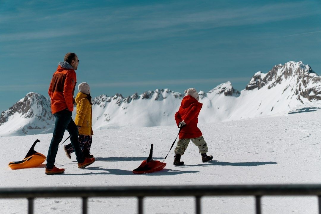 Family carrying sleds across a snowy Alpine landscape