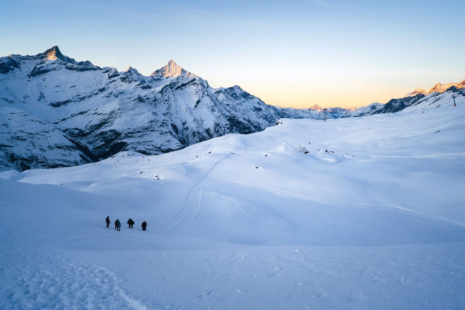Snowshoers crossing a marked alpine trail beneath snowy peaks